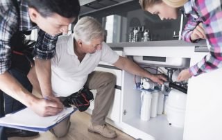 Licensed plumber inspecting under-sink plumbing during a kitchen remodel