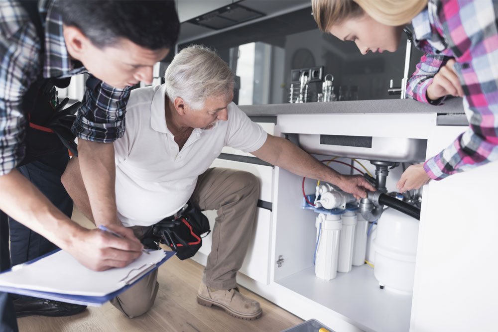 Licensed plumber inspecting under-sink plumbing during a kitchen remodel